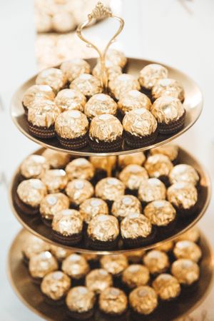 Three-tiered serving tray filled with gold-wrapped Ferrero Rocher chocolates for elegant party display.