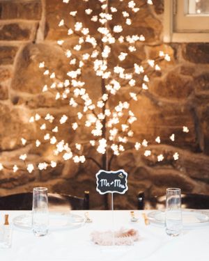 Romantic table setting with glowing string lights against rustic stone wall and chalkboard sign.