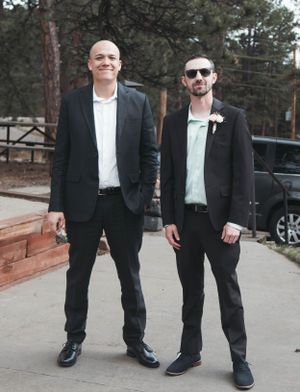 Two men in black suits and white shirts pose together outdoors for formal event photo.