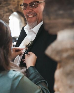 A boutonniere being pinned on a formal black suit jacket during wedding preparations.