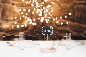 Wedding reception table with Mr & Mrs sign and string lights glowing against stone wall backdrop.