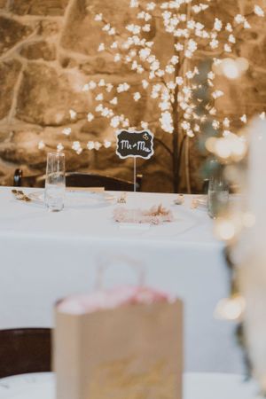 Wedding reception table with string lights and Mr & Mrs sign against stone wall.