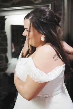 Side profile view of someone in a white lace wedding dress with an updo hairstyle and pearl earring.