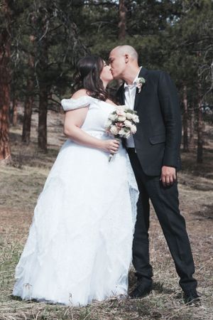 A romantic wedding moment captured in a forest setting with pine trees in the background.