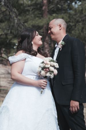 A joyful wedding couple shares an intimate moment outdoors while the bride holds a bouquet of roses.