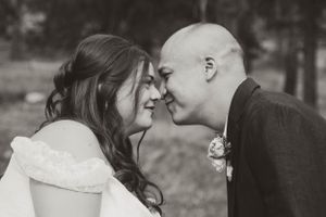 Black and white romantic wedding photo showing a tender moment between a couple touching foreheads outdoors.