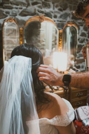 A bride getting her veil adjusted in front of vintage mirrors with stone walls in the background.