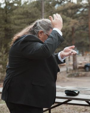 Wedding guest in formal attire reacting emotionally during outdoor ceremony.