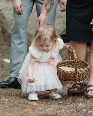 A small child in a pink tulle dress bends down near a wicker basket.