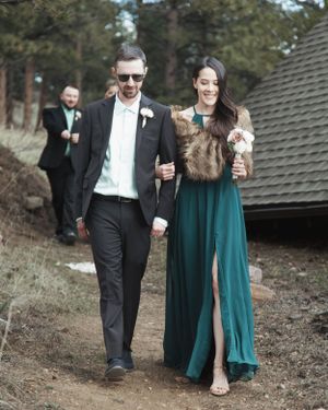 A couple walks arm in arm outdoors, with the woman wearing a green dress and fur stole.