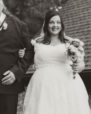 A bride in a beautiful white wedding dress holds a floral bouquet during an outdoor ceremony.