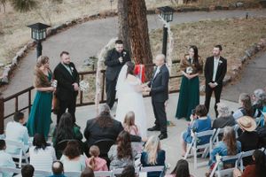 Aerial view of outdoor wedding ceremony with guests seated in white chairs and emerald green decor.