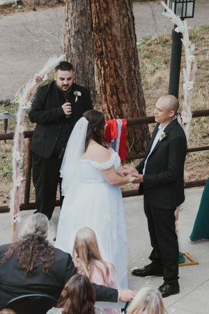 Outdoor wedding ceremony taking place under a tree with an officiant and couple exchanging vows.