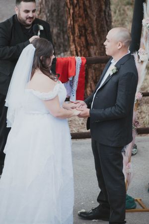 Wedding ceremony in progress with couple holding hands while officiant presides under trees.