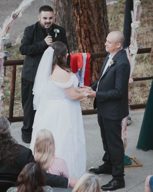 A wedding ceremony taking place outdoors with an officiant and couple surrounded by guests and trees.