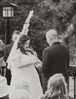 A wedding ceremony taking place outdoors with a decorative lamp post and trees in the background.