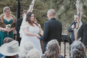 An outdoor wedding ceremony taking place with attendees seated and watching a couple exchange vows under trees.