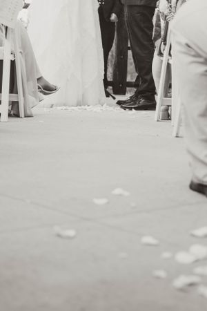 Black and white photo of wedding guests' feet and flower petals scattered on the ground during ceremony.