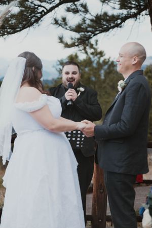 A winter wedding ceremony takes place outdoors with snow-covered trees in the background.
