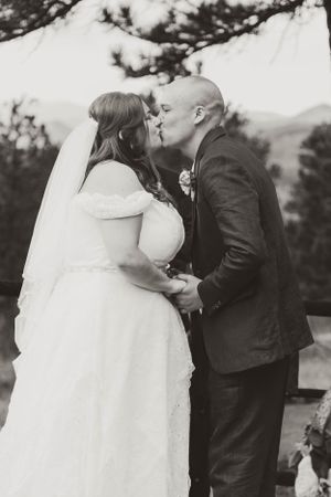 A romantic black and white wedding photo of a couple sharing their first kiss during an outdoor ceremony.