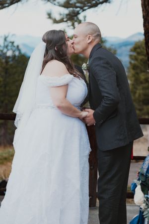 A couple sharing their first kiss during an outdoor mountain wedding ceremony.