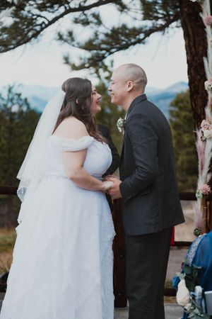 A bride and groom hold hands during their outdoor wedding ceremony with mountain views.