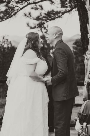 A black and white portrait captures a tender moment between newlyweds in a forest setting.
