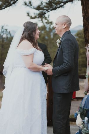 A couple shares a joyful moment during their outdoor wedding ceremony while holding hands.