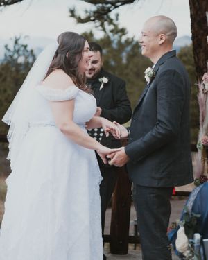 An intimate outdoor wedding ceremony with a couple exchanging rings under pine trees.