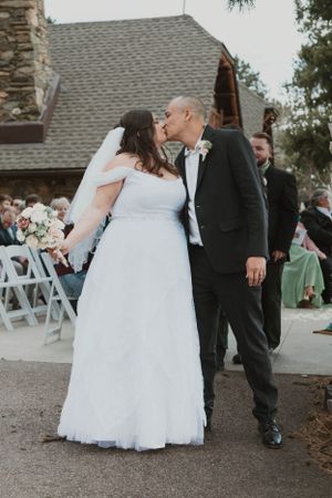 A couple shares their first kiss as newlyweds at an outdoor wedding ceremony.