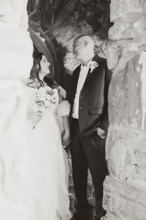 A romantic black and white wedding photo of a couple standing against a stone wall.