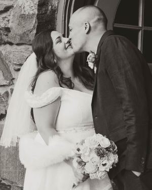 A romantic black and white wedding photo showing a couple kissing while the bride holds a beautiful rose bouquet.