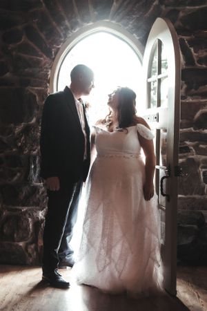 A romantic silhouette of newlyweds standing in a stone archway filled with bright natural light.