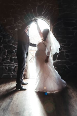 Silhouetted bride and groom stand in stone archway with dramatic backlight creating romantic wedding moment.