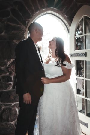 A romantic wedding moment captured in an arched stone doorway with natural backlighting creating a dreamy atmosphere.