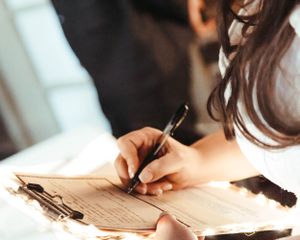 Close-up shot of hands signing documents with a pen on paper.