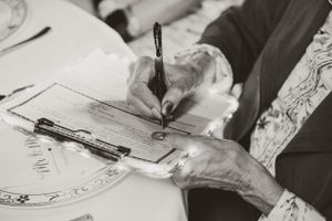 Black and white image of hands signing official documents at a formal event.