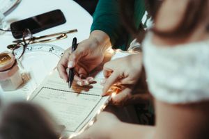 Close-up of hands signing marriage documents on a table.