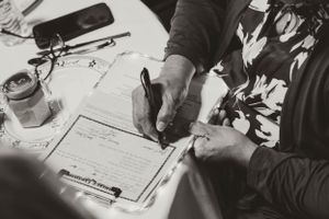 Black and white close-up of hands signing marriage documents with a pen.