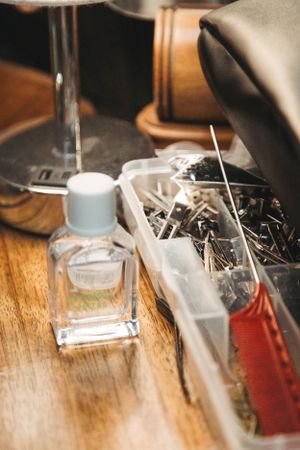 Hair styling tools and products arranged on a wooden surface with a glass bottle and pins in clear containers.