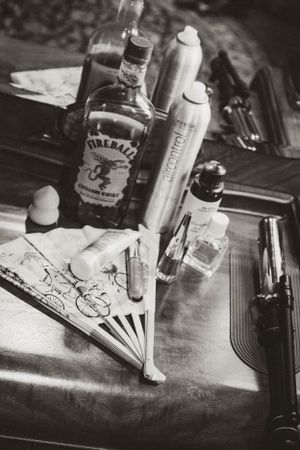 Black and white still life with Fireball whiskey bottle, spray cans, and a decorative fan on a dark surface.
