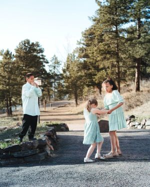 A family in coordinating mint outfits poses on a mountain path surrounded by tall pine trees.
