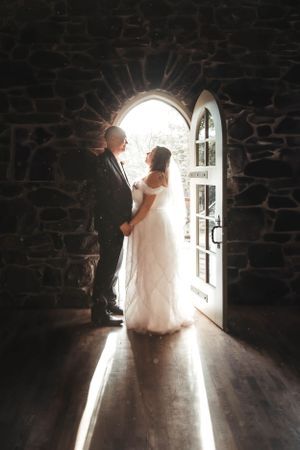 A silhouetted couple stands in an arched stone doorway with bright sunlight streaming in behind them.