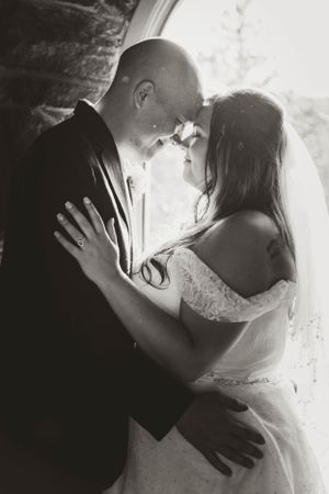 A romantic black and white portrait of newlyweds embracing in a stone archway.
