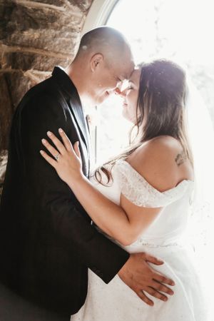 An intimate wedding portrait showing a couple sharing a tender moment against a stone wall backdrop.