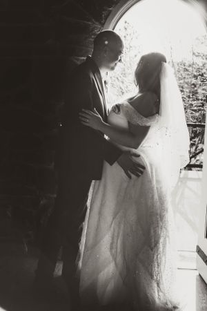 A romantic black and white wedding photo of a couple embracing in dramatic side lighting.