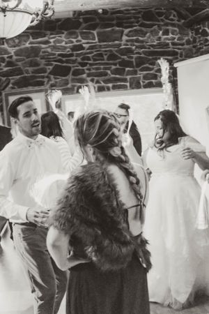 A lively dance party scene at a rustic stone-walled venue with guests in formal attire.