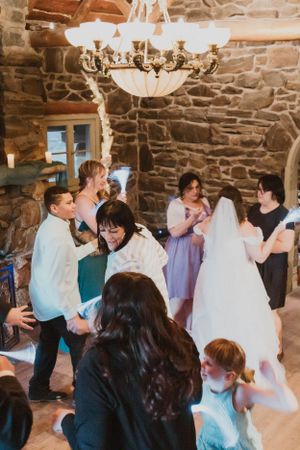 Wedding guests dance and celebrate in a rustic stone-walled venue under elegant chandeliers.