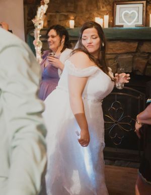 Wedding reception scene showing guests dancing and celebrating in a rustic venue with stone fireplace.