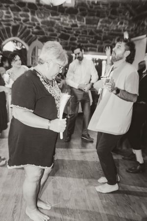 Black and white photo of people dancing and having fun at a party in a stone-walled room with wooden floors.